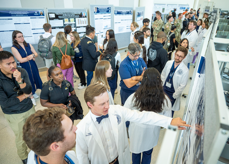 People wearing lab coats and casual clothes chat and look at research poster presentations.