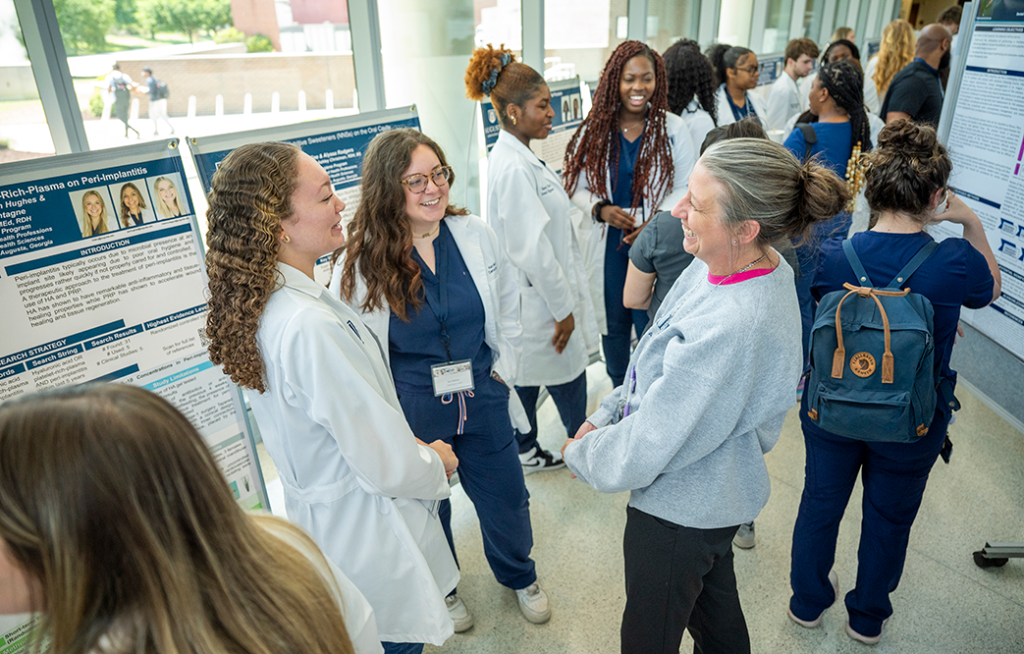 A group of women chat and laugh in front of poster presentation at a dental research symposium.