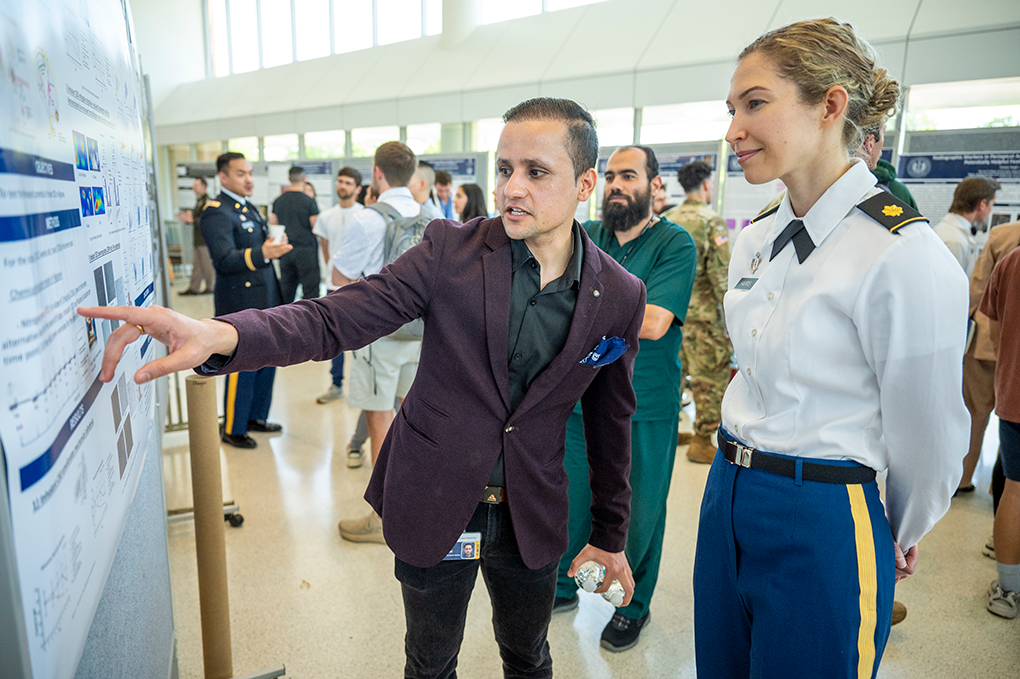 A man points to a research poster and explains it to a woman wearing a military uniform.