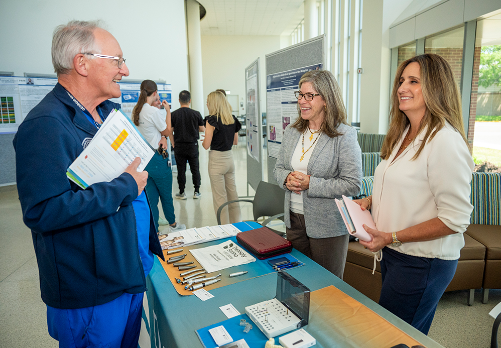 Two women at a sponsor booth speak with man wearing scrubs.