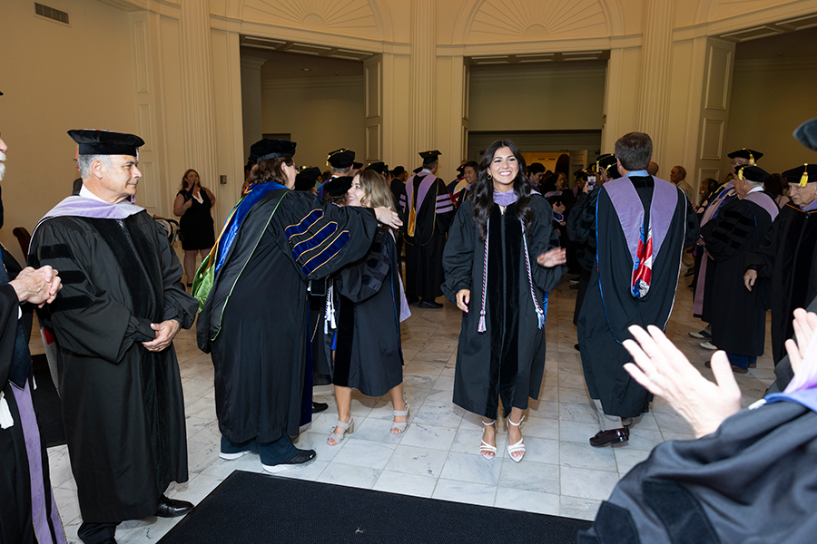 College graduates in full graduation regalia celebrates with their professors, also dressed in full college regalia.