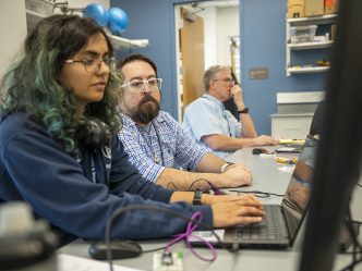 Woman working on a computer sitting next to two men
