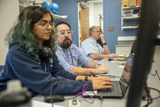 Woman working on a computer sitting next to two men