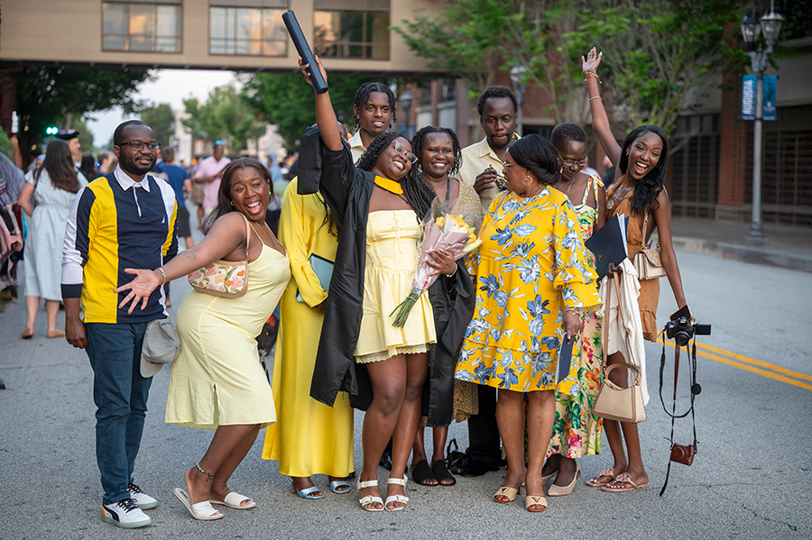A large family gathers around a college graduate and cheer to celebrate her achievement.