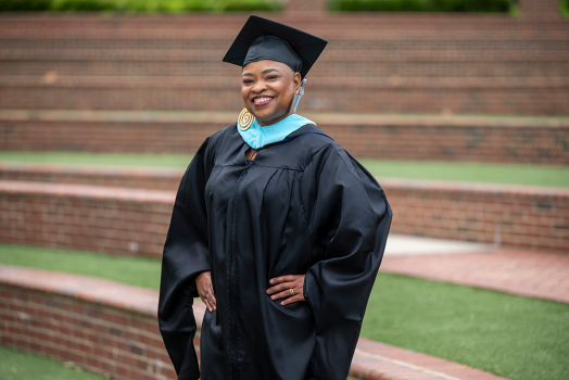 Woman wearing square hat with hands on her hips stands in front of brick stairs.