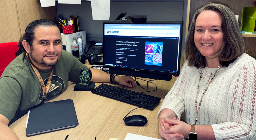 Two college professors sit beside a computer monitor with an online textbook pulled up.