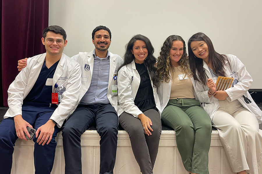 Five medical students, three women and two men, sit on a stage.