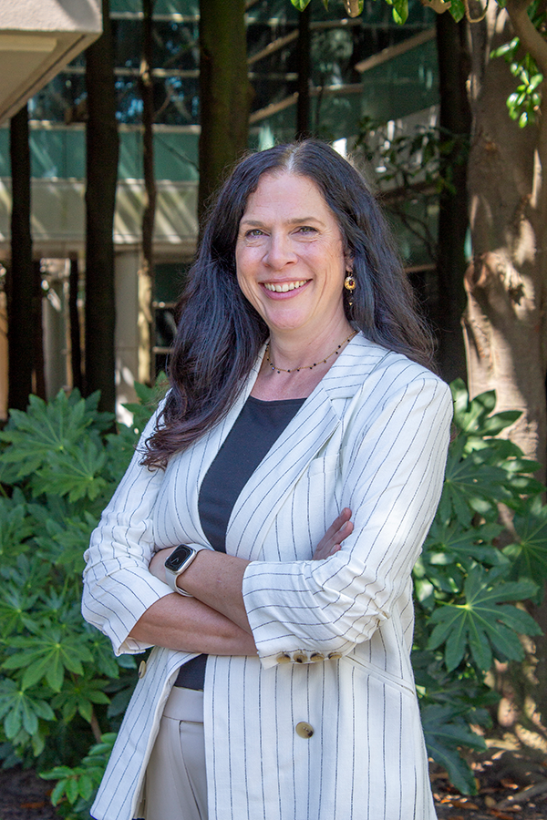 A female college professor standing outside of a large research building.