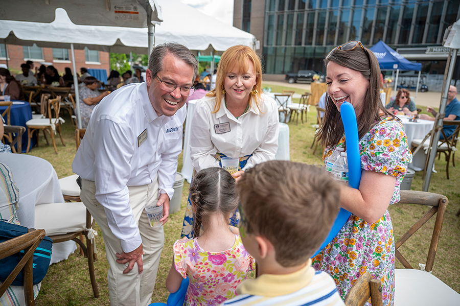 A man and a woman greet two children and their mom during a big outdoor event.