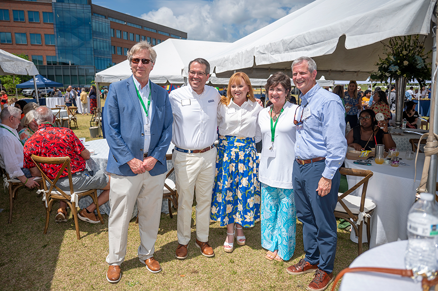 Three men and two women stand and talk during a big outdoor event.