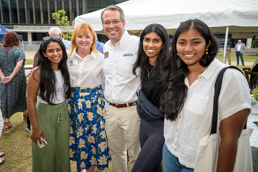A man and his wife stand with three female college students during a large outdoor event.