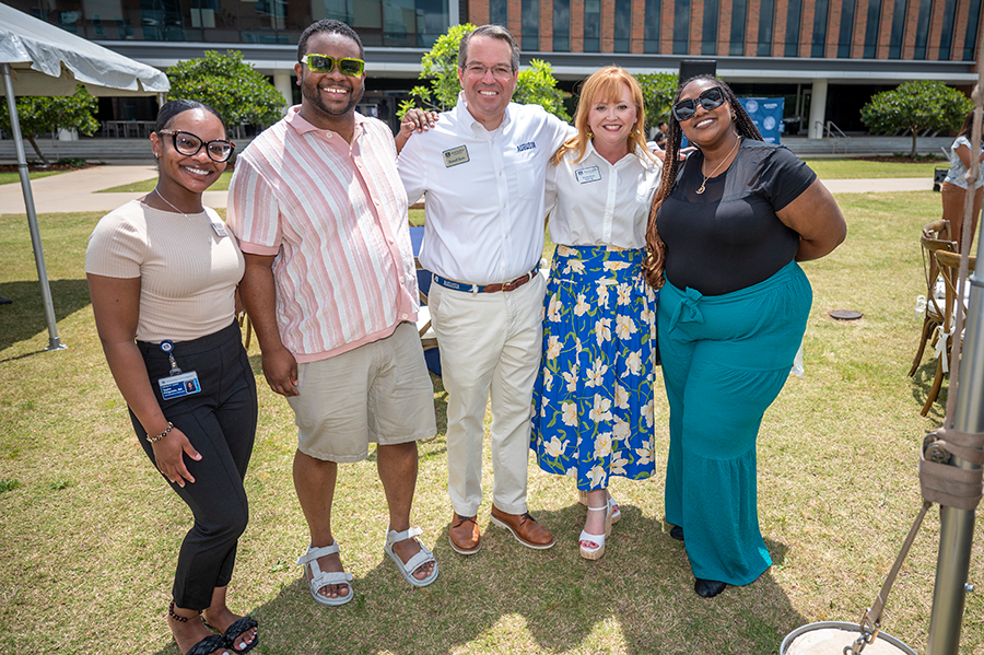 A man and his wife stand with three younger adults during a large outside event.
