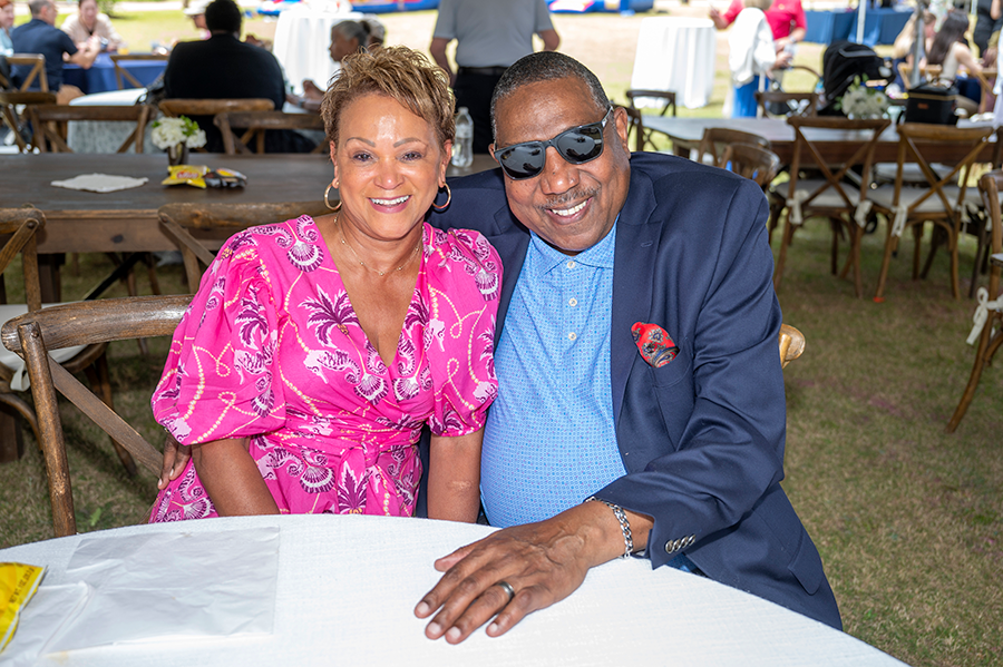 A man and a woman sit at a table outside during a big event.