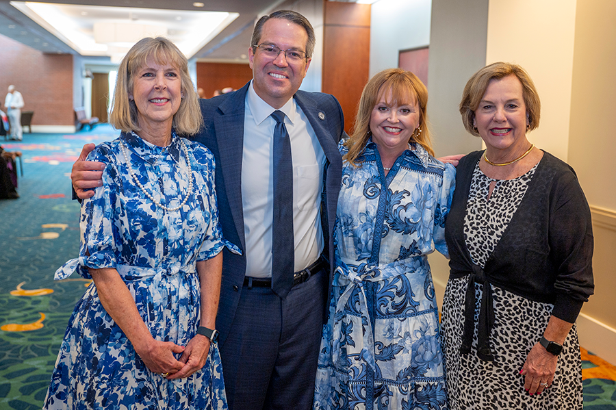 Three women stand with a man in a large hallway just before a large event.