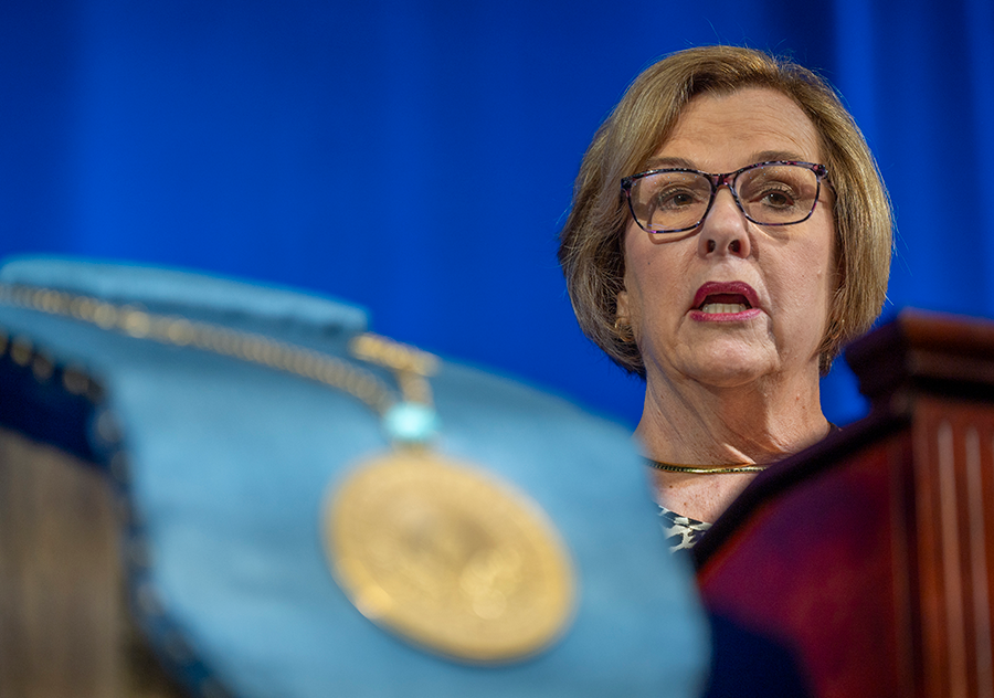 A woman stands at a podium with a microphone and delivers a speech to a large group of people.