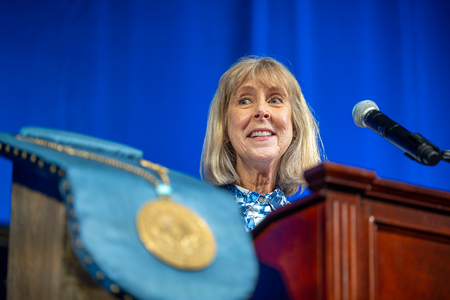 A woman stands at a podium with a microphone and delivers a speech to a large group of people.