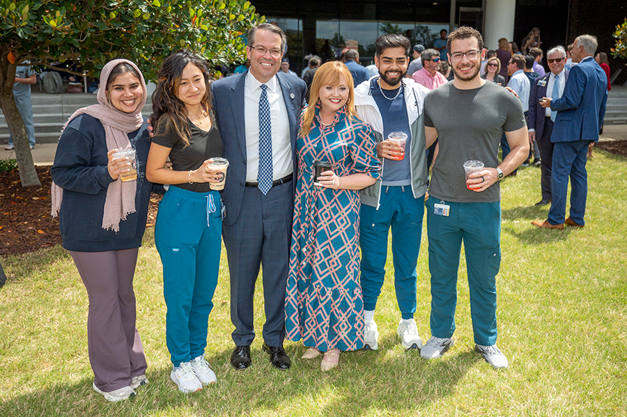 Four college students stand and talk to a college president and his wife. They are outside and everyone is holding a cup of coffee.