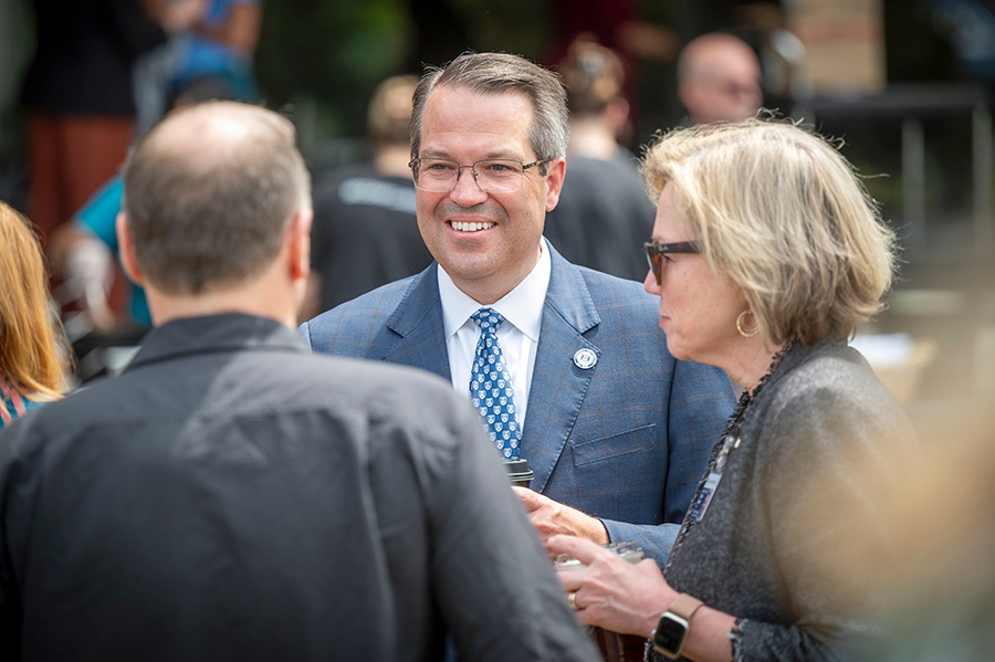 A man in a suit and tie speaks with a small group of people outside at an event.
