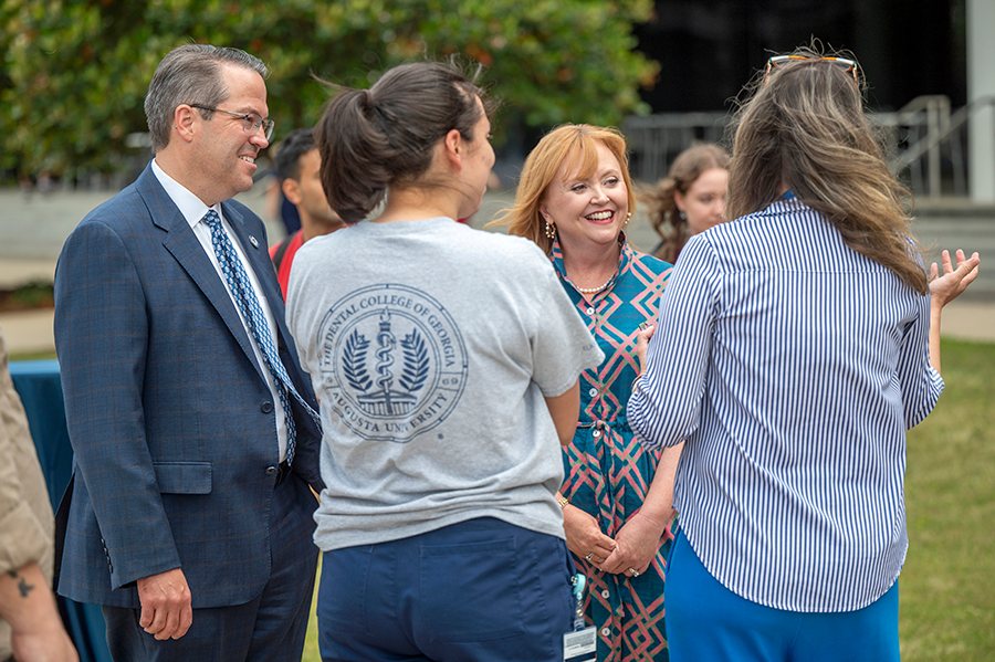 A man and a woman meet with a college student and a professor during an outside event at a college campus.