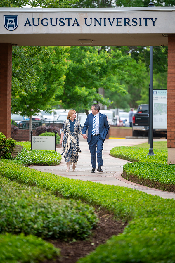 A man and his wife walk hand-in-hand along a path on a college campus.