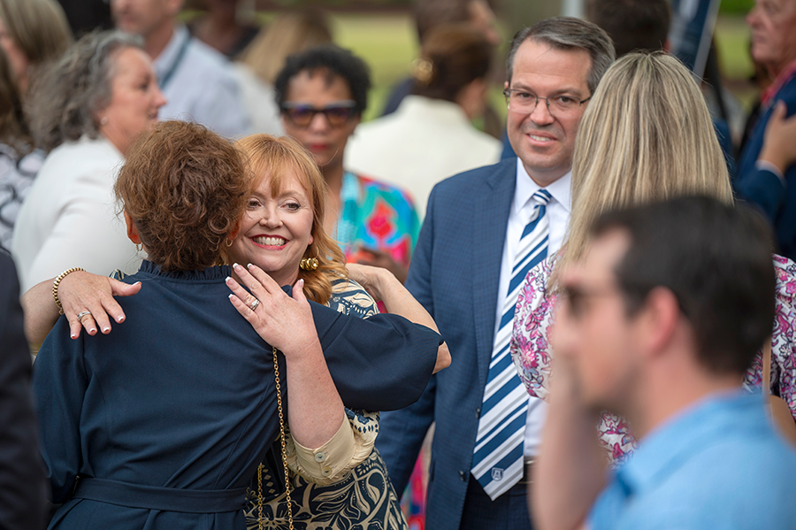 Two women hug during a greeting at a large outdoor event.