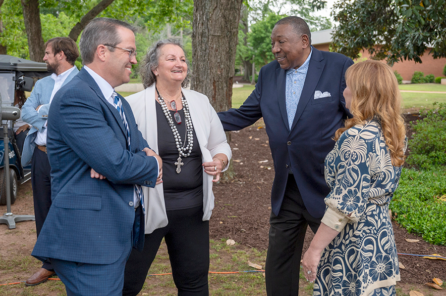 Two women and two men talk under the shade of a tree during an outside event.