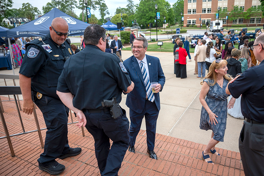 A man wearing a suit and tie greets two police officers and shakes their hands.