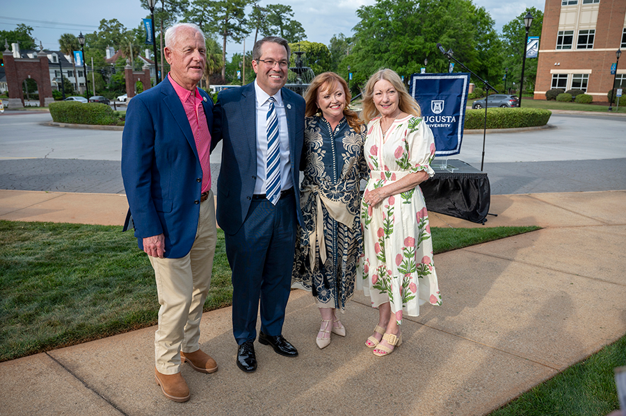 Two women and two men stand in front of a stage during a special event on a college campus.