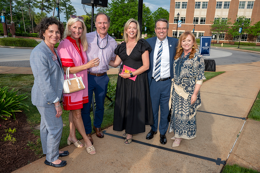 Four women and two men stand outside on a college campus during a special event.