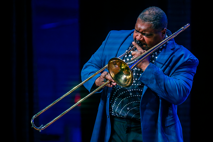 A man plays the trombone on a stage during a large musical performance.