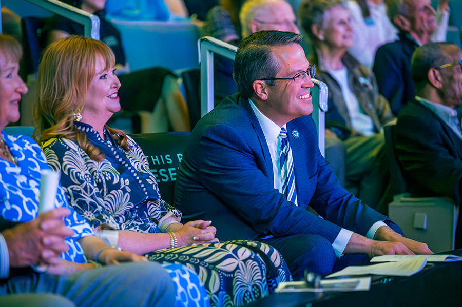 A man and his wife smile as they listen to a musical performance in a theater.