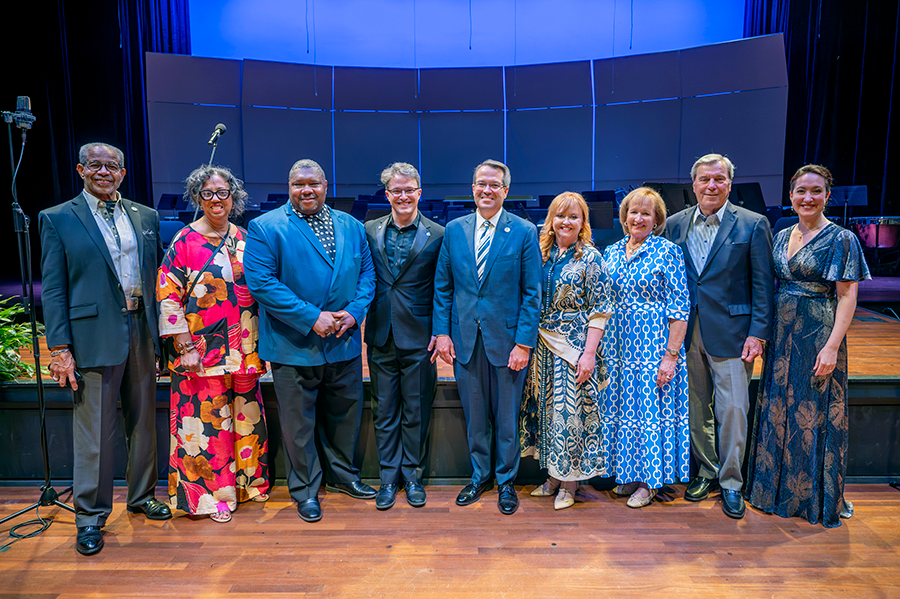 A group of men and women stand together on a stage following a musical performance in a large theatre.