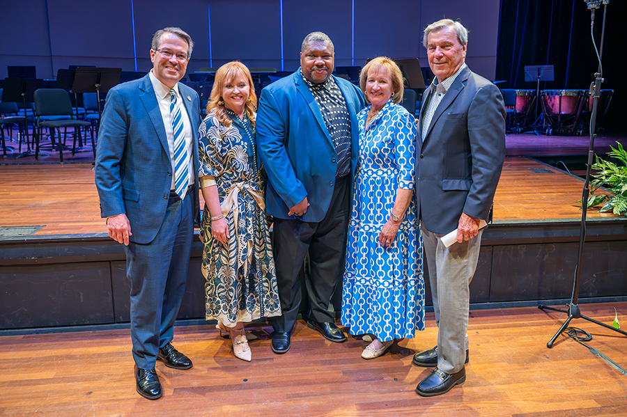 Three men and two women stand together following a musical performance in a large theater.