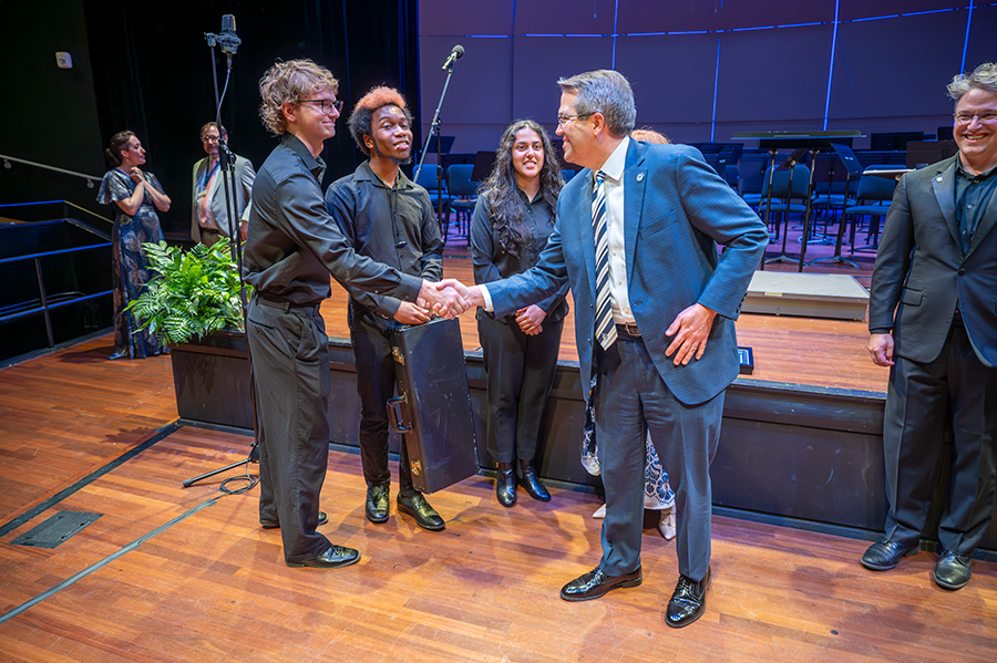 A man shakes hands to greet a college student while two other students look on.