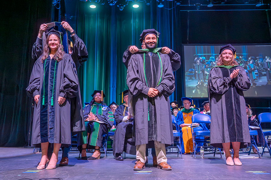 Two medical school graduates, one man and one woman, have their ceremonial hoods placed around their shoulders during a hooding ceremony.