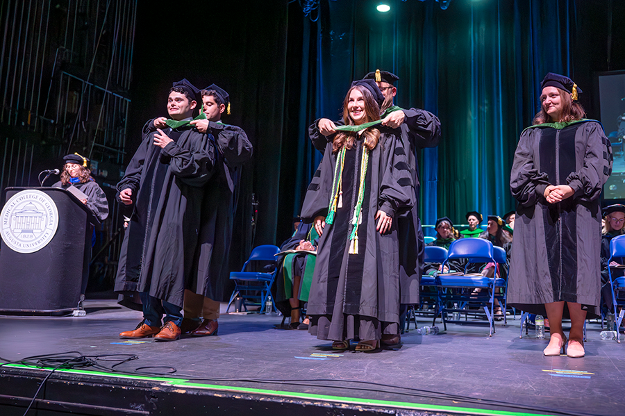 Two medical school graduates, one man and one woman, have their ceremonial hoods placed around their shoulders during a hooding ceremony.