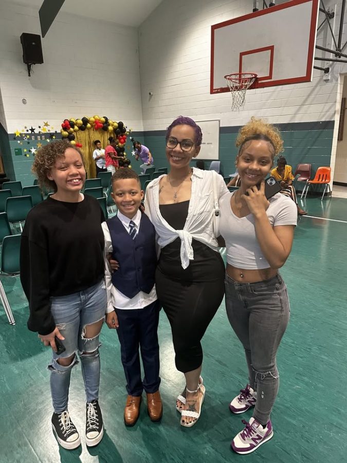 A woman poses with her three children in a gym with chairs ready for a ceremony