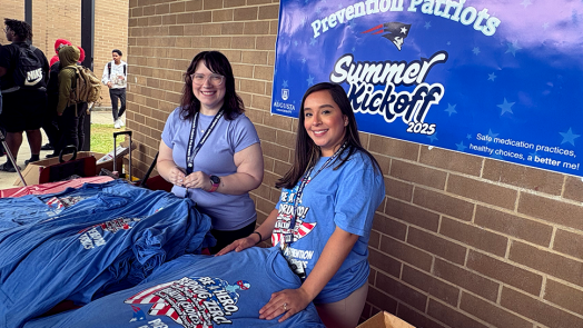 Two women smile while handing out t-shirts advocating for drug misuse prevention.