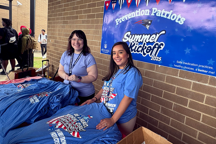 Two women smile while handing out t-shirts advocating for drug misuse prevention.