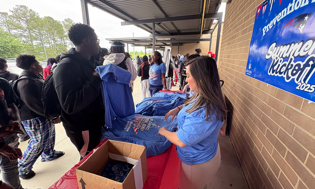A woman hands out t-shirts advocating for drug misuse prevention to high school students.