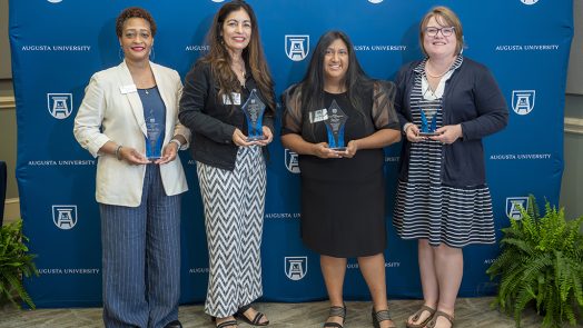 Four women smiling while holding awards