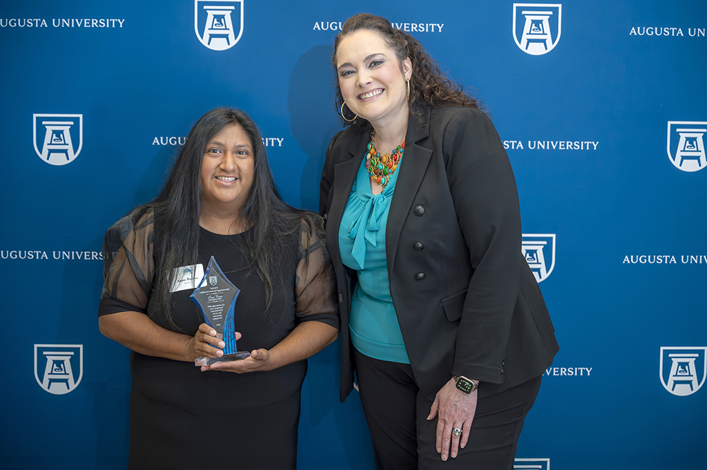 Two women posing for a photo with an award