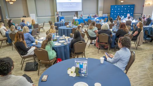 Men and women sitting at tables listening to a speaker