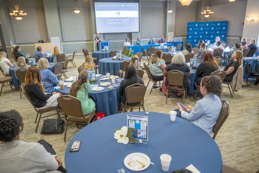 Men and women sitting at tables listening to a speaker
