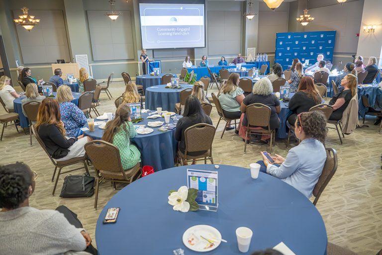 Men and women sitting at tables listening to a speaker