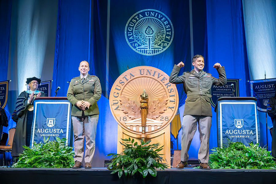 A male Army ROTC cadet flexes his muscles to celebrate swearing into the U.S. Army. He is wearing full cadet dress.