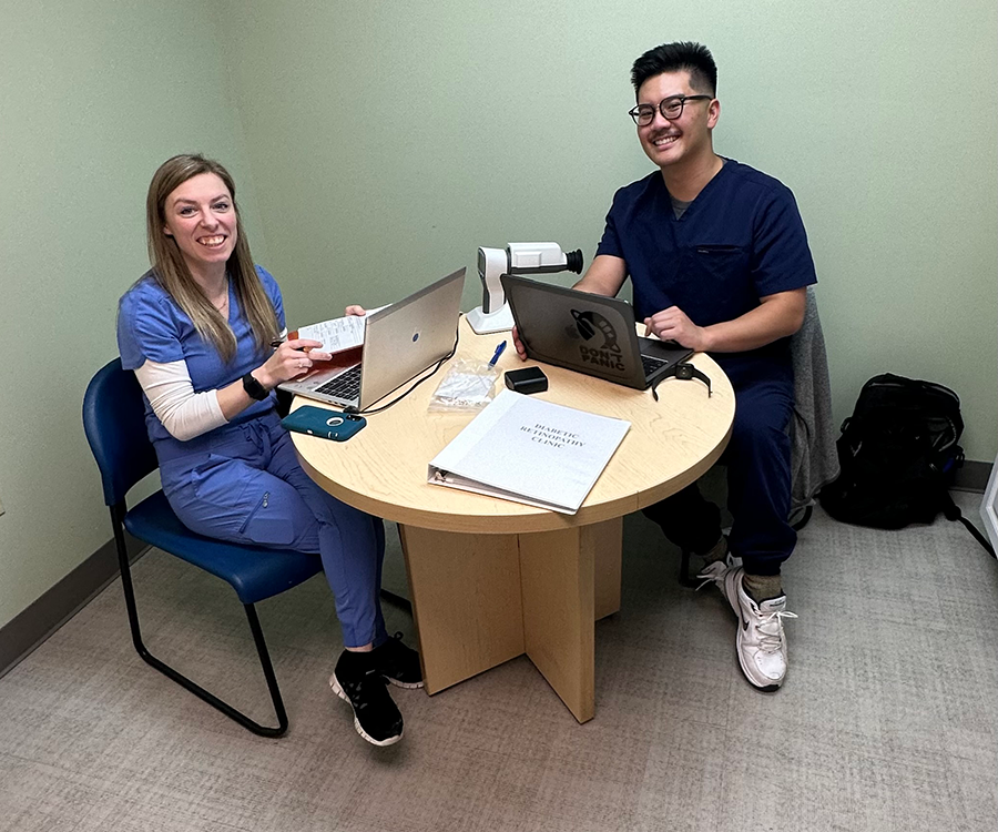 A male and a female medical student sit at a table with a pair of laptops and look over data.