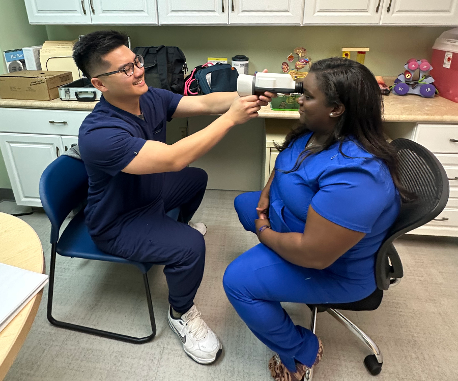A male medical student practices using a special camera that takes pictures of a person's eye on a fellow medical student.