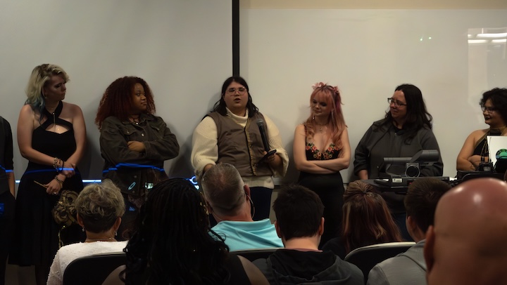 A group of college students stand at the front of a classroom and speak during a question and answer session.