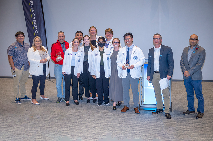 A group of 8 medical students gather for a team photo after a competition. They are joined for the celebratory photo by members of the judging panel.